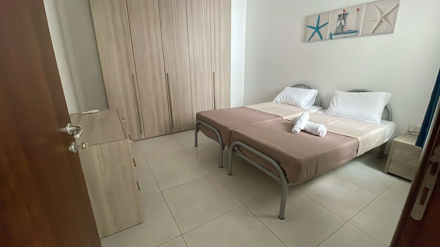 Twin bedroom with crisp white pillows, beige linens and seaside artwork