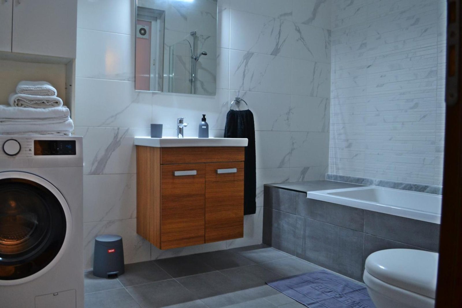 Marble-tiled bathroom with bathtub, vanity and washing machine